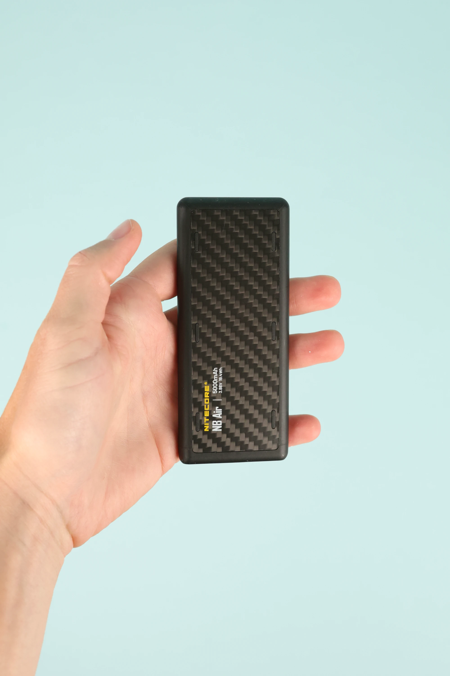 Hand holding the Nitecore NB Air Powerbank with a sleek, compact design on a light blue background.