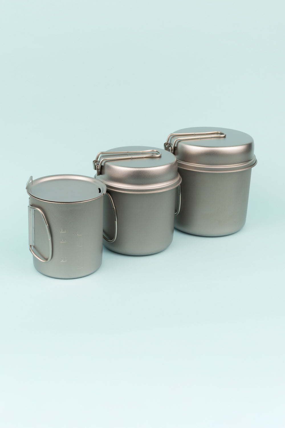 Snow Peak Nesting Pot Set featuring three titanium pots with foldable handles against a mint background.