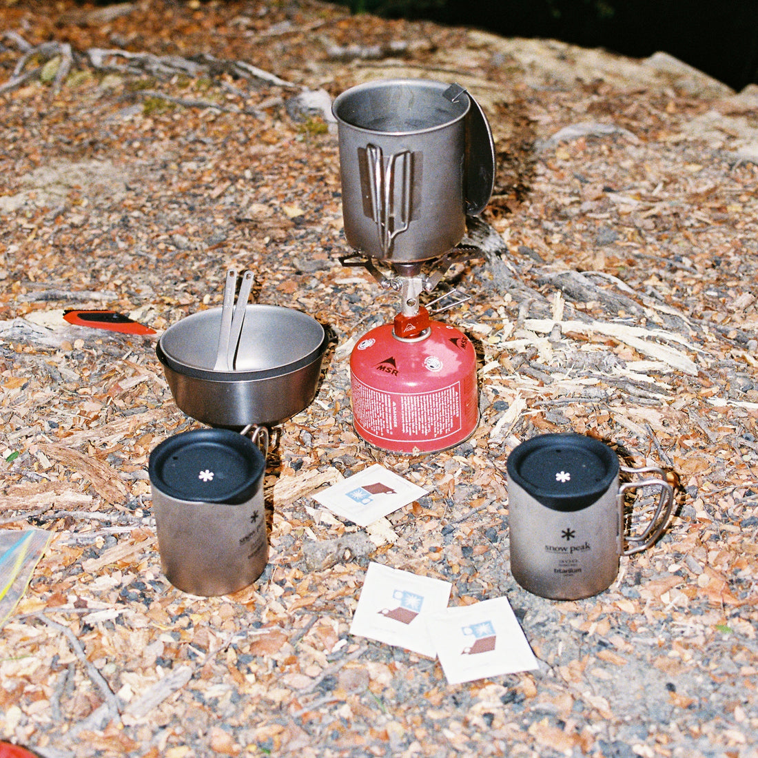 Camping setup with cookware and Japanese-inspired mugs on the ground.