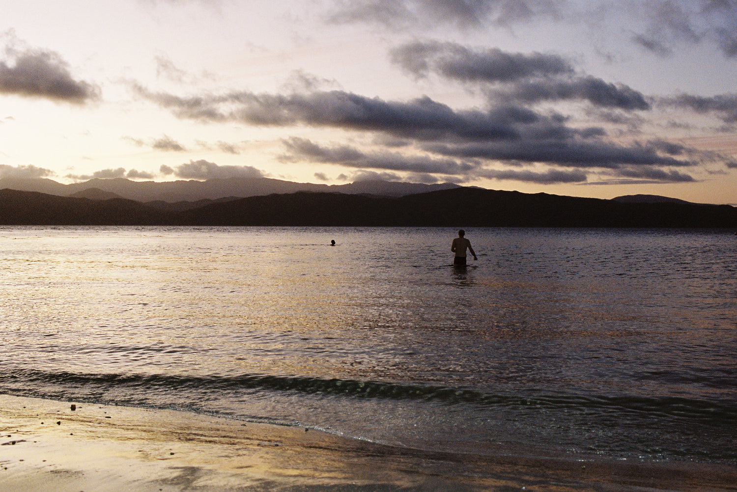 Person enjoying Coffee Outdoors by the beach at sunset, with calm water and distant mountains.