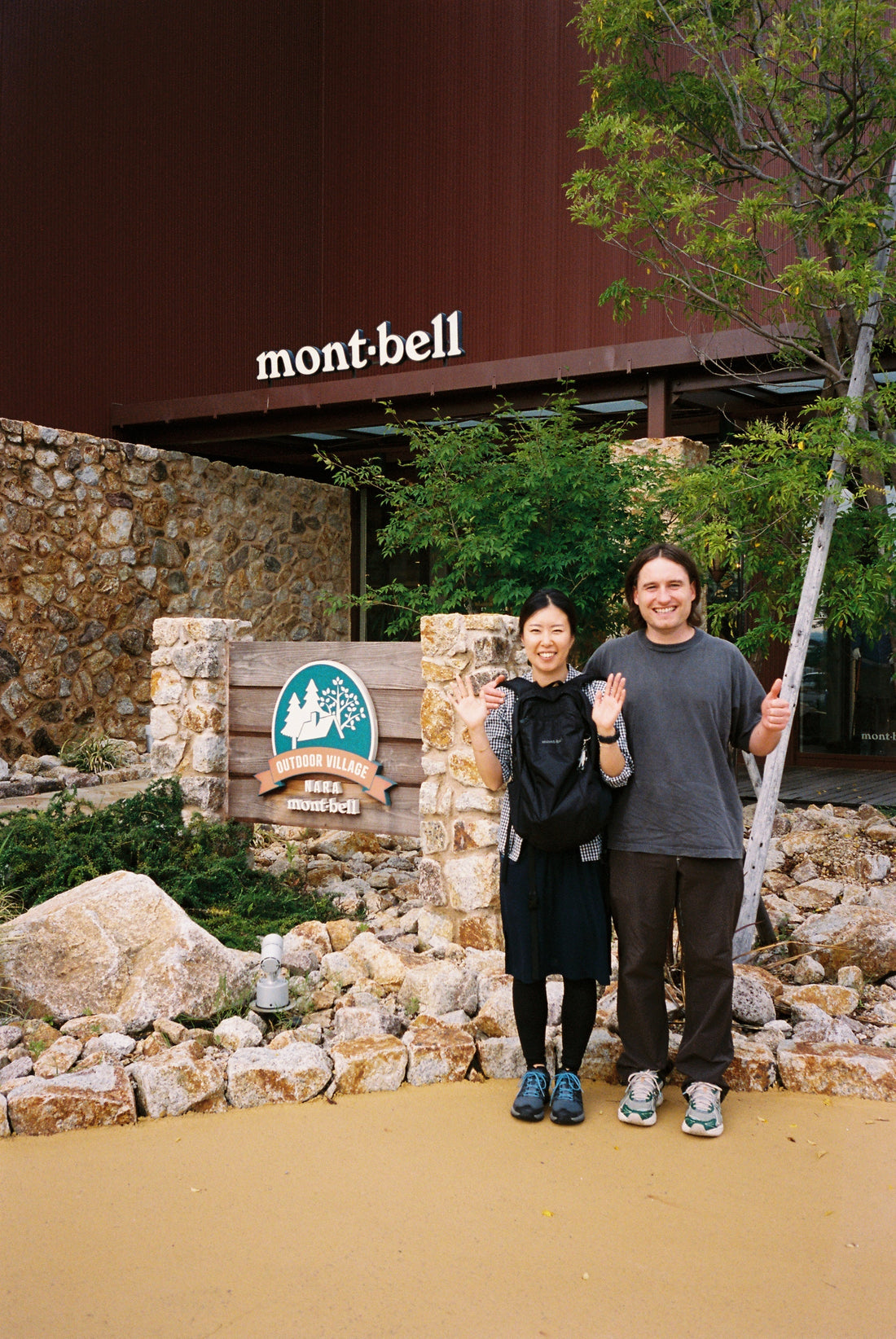 Couple posing in front of Montbell store sign, excited to meet and explore outdoor gear.