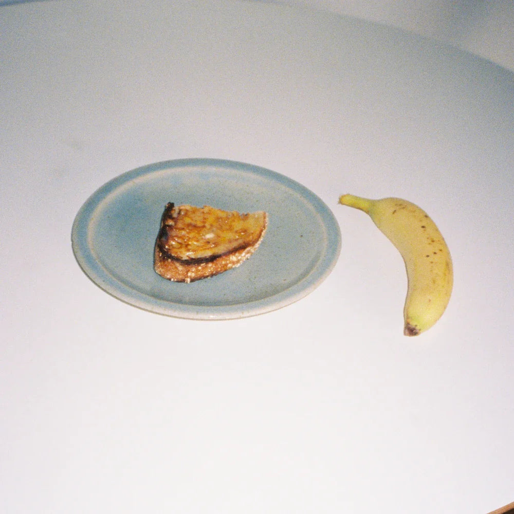 A slice of toast on a blue plate next to a banana, showcasing a simple breakfast scene.