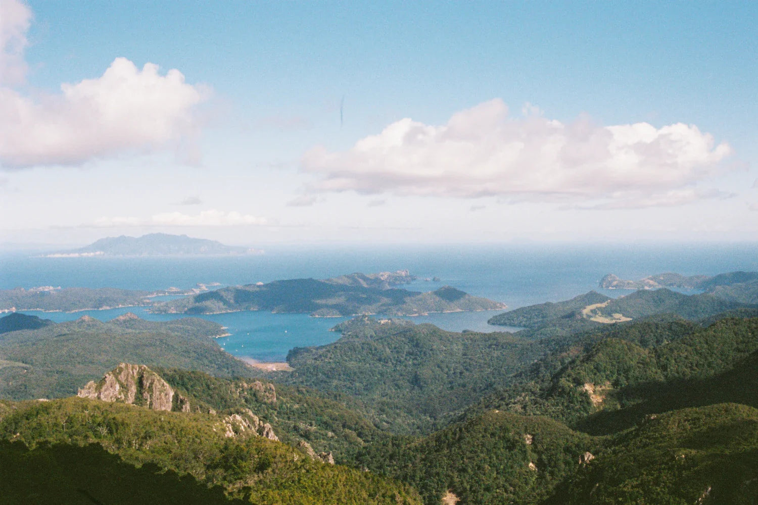 A panoramic view of Aotea showcasing lush greenery and coastal waters under a bright blue sky.