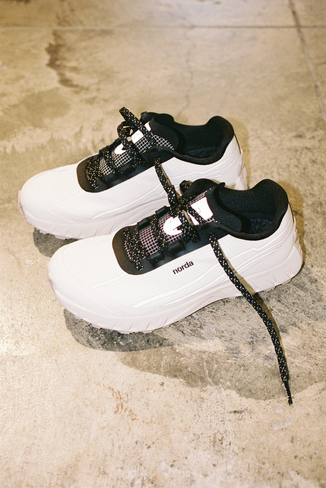 Stylish white Norda sneakers with black laces on textured floor.