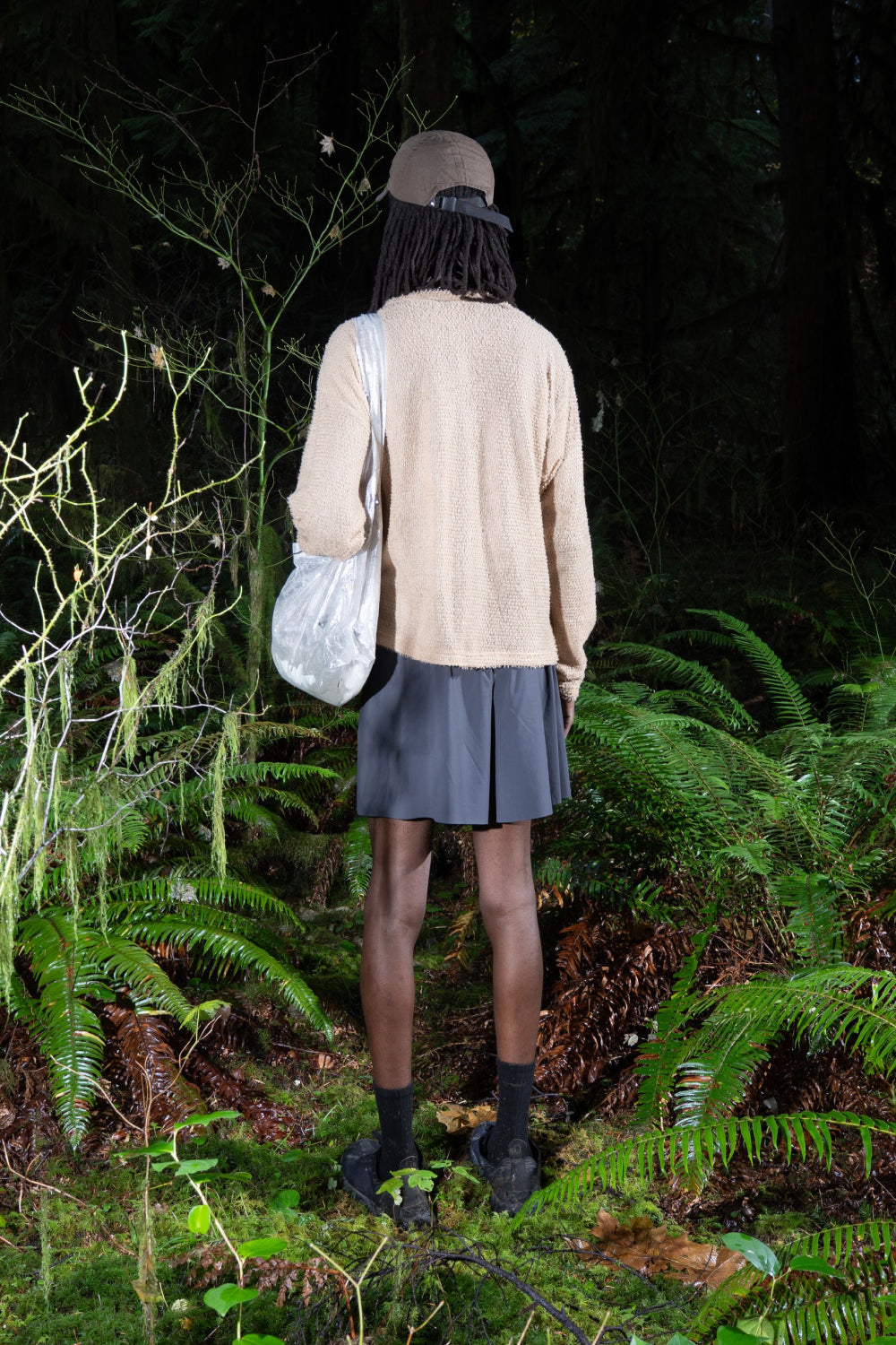 Person wearing Shag Sweater v2.0 in cornstalk color, standing in a forest with ferns and carrying a bag.