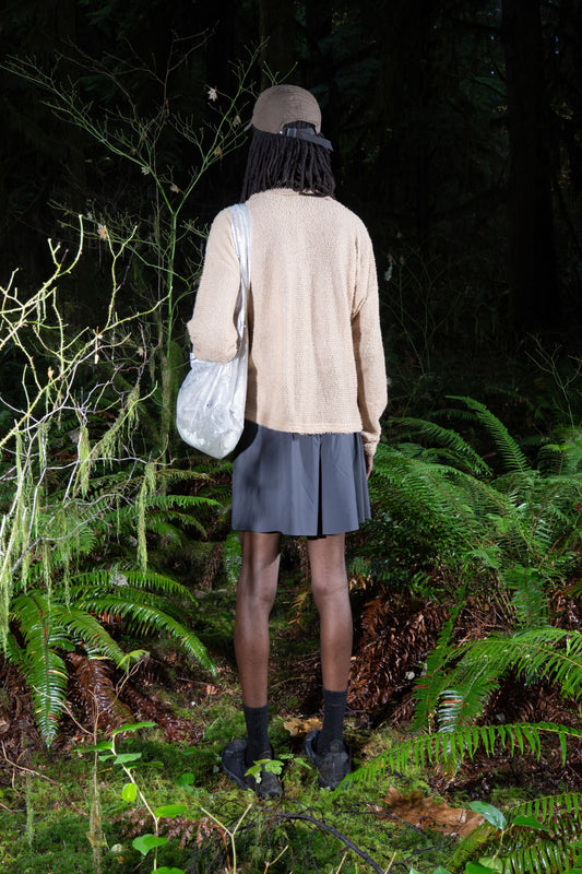Person wearing Shag Sweater v2.0 in cornstalk color, standing in a forest with ferns and carrying a bag.