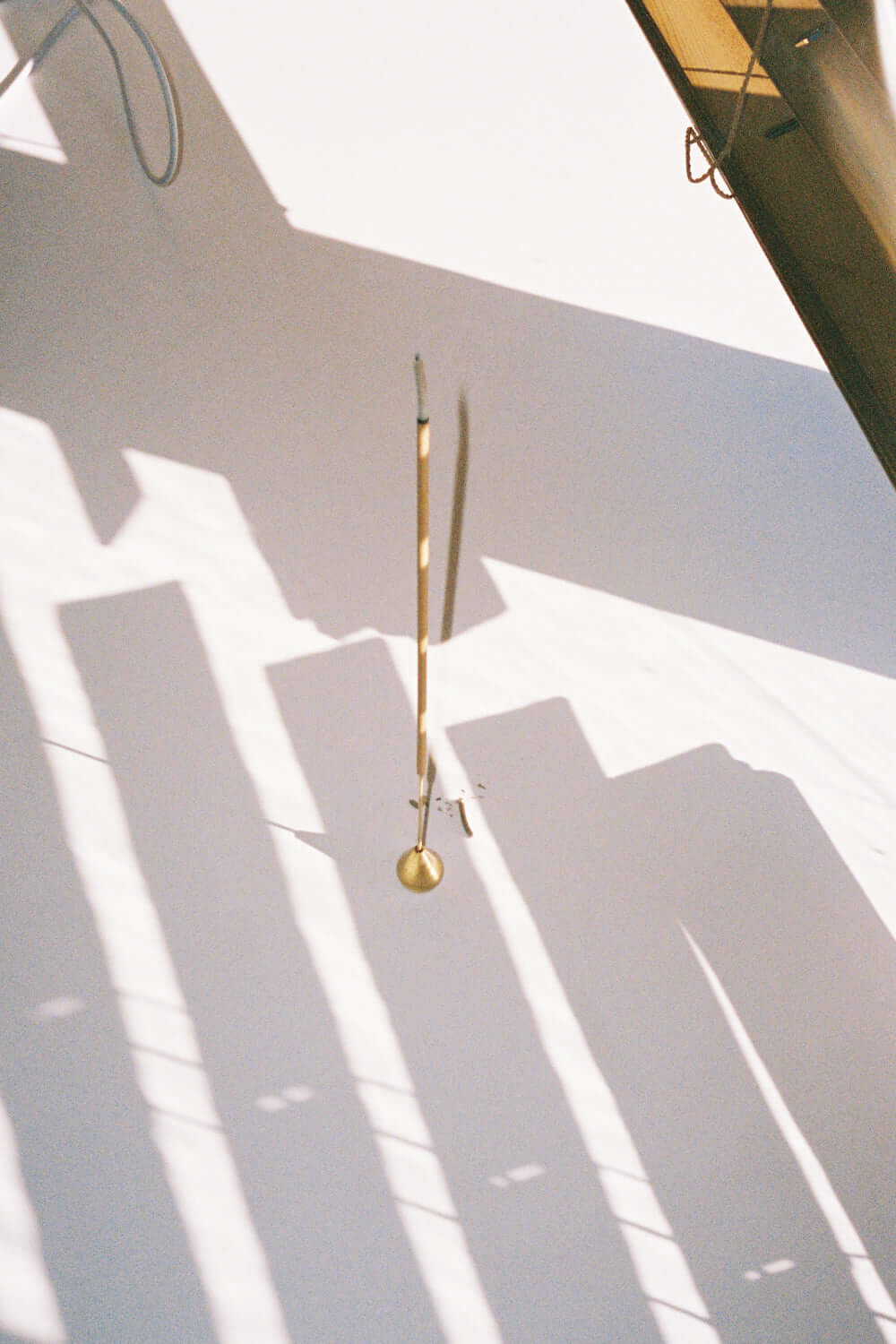 Hazza Hana Incense stick hanging with shadows on a white wall, showcasing an elegant design.