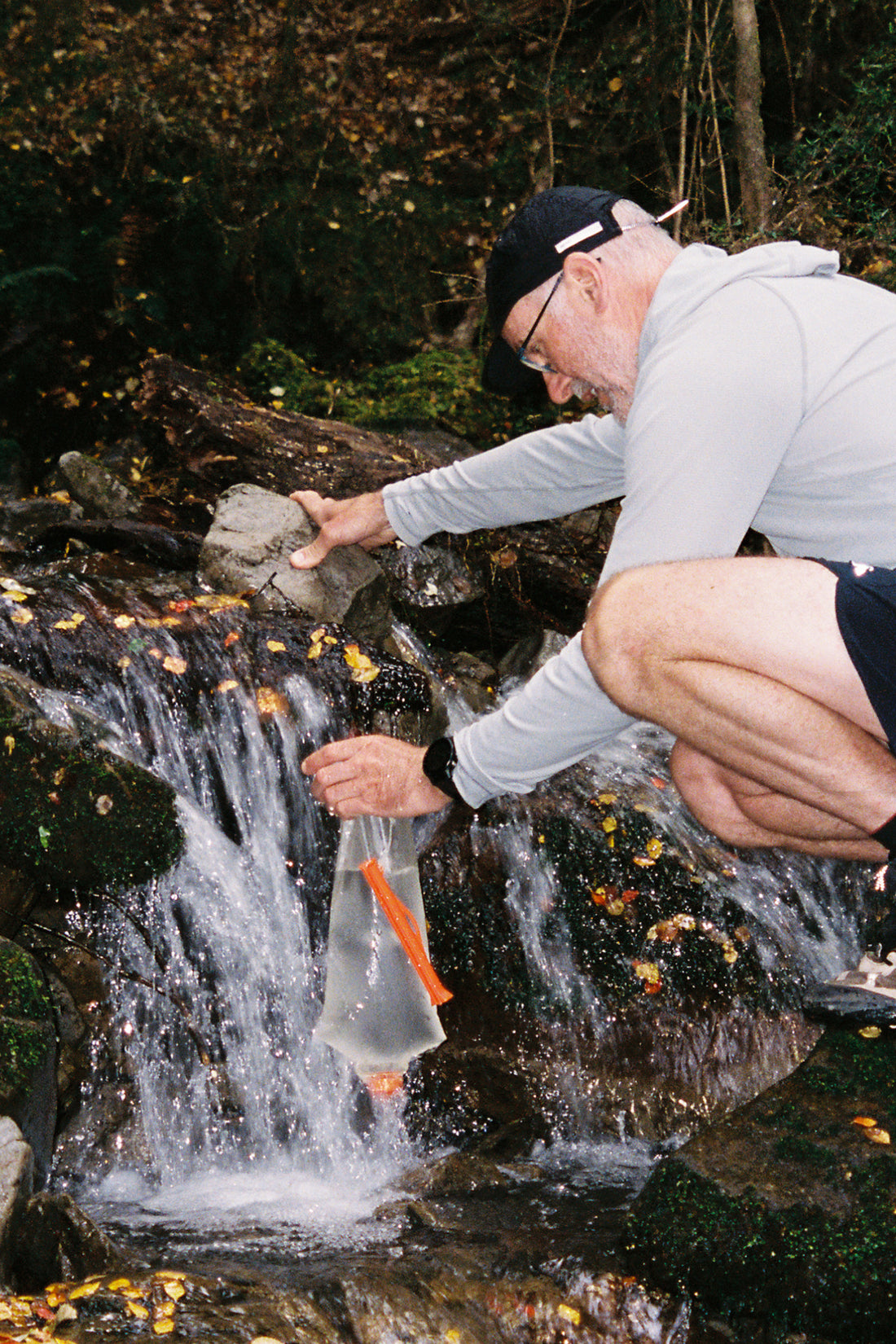 Person filling the Vecto 2L Water Bladder in a stream surrounded by autumn leaves.