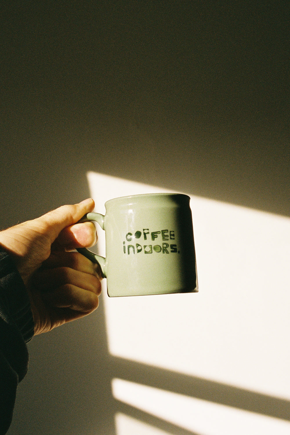 Coffee Outdoors x Taus Diner Cup - Green held in hand with sunlight highlighting its ceramic finish.