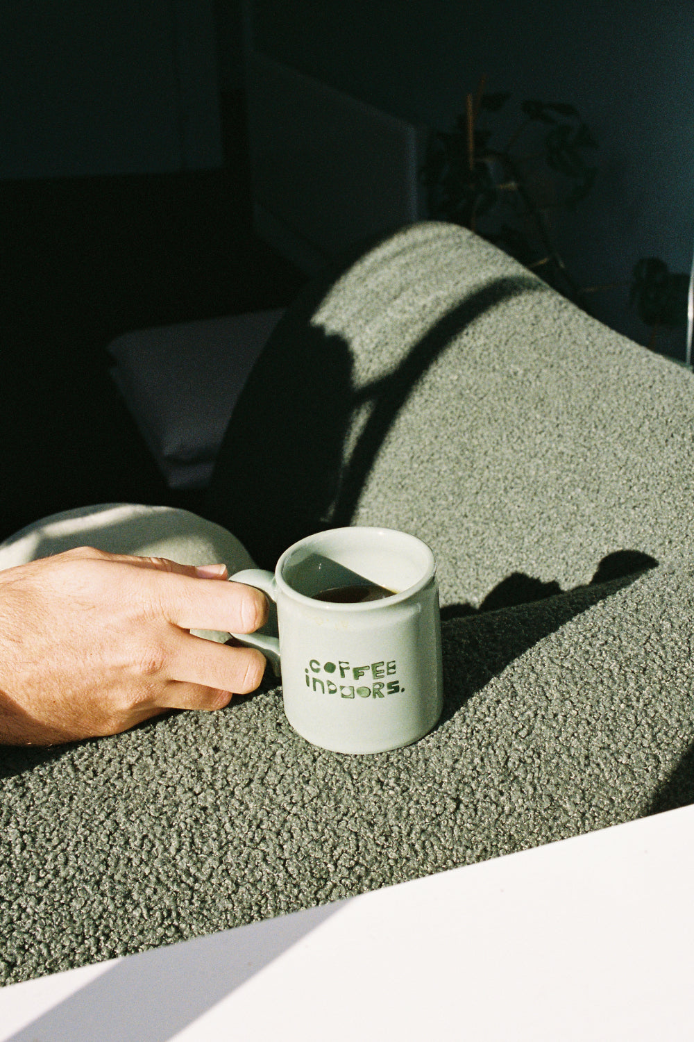 Coffee Outdoors x Taus Diner Cup - Green on a textured surface with a hand holding it.