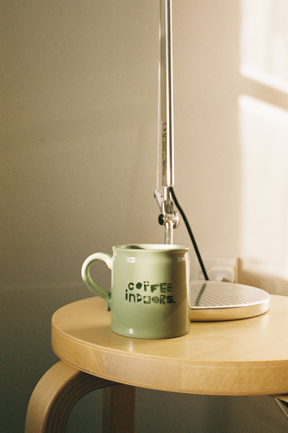 Coffee Outdoors x Taus Diner Cup - Green on a wooden table next to a lamp, showcasing its clean lines and handcrafted design.