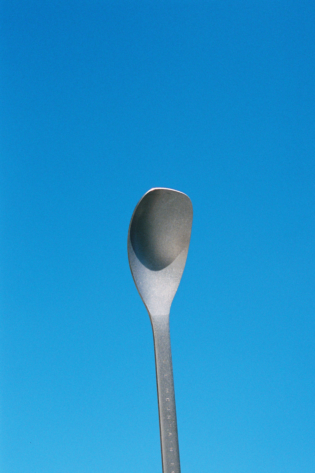 SputuraTi long handle spoon against a clear blue sky, ideal for outdoor cooking and reaching into deep pots.