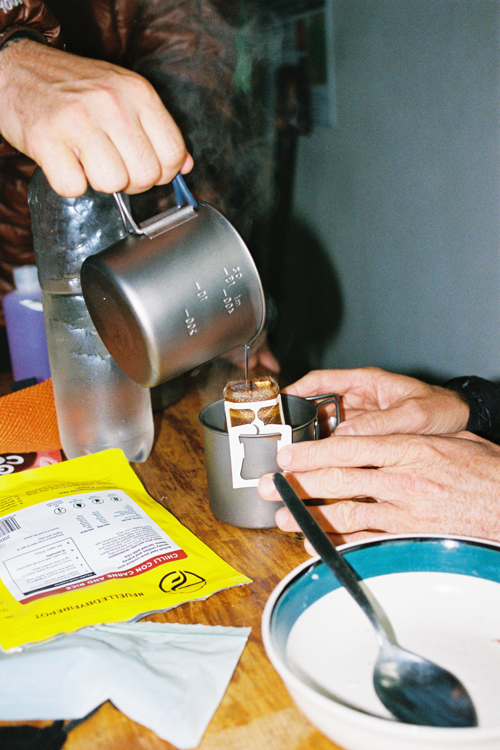 Pouring hot beverage from MP500 Flat Titanium Pot into a cup with a person’s hands and water bottle in view.