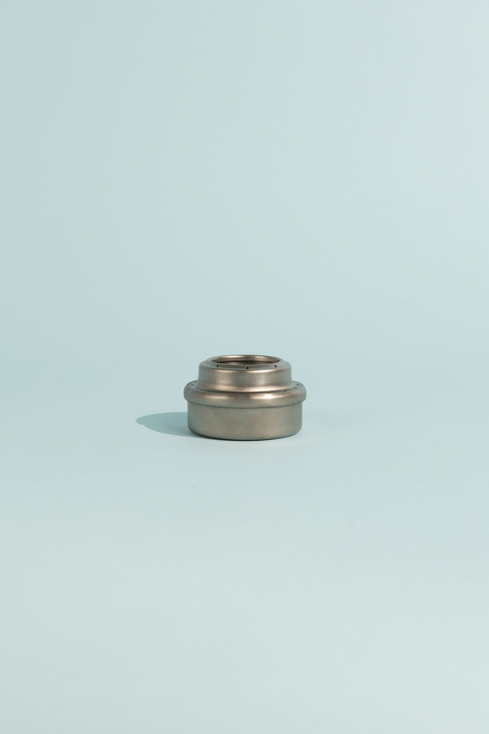 Evernew Titanium Alcohol Stove on a light blue background, showcasing its compact and sleek design.