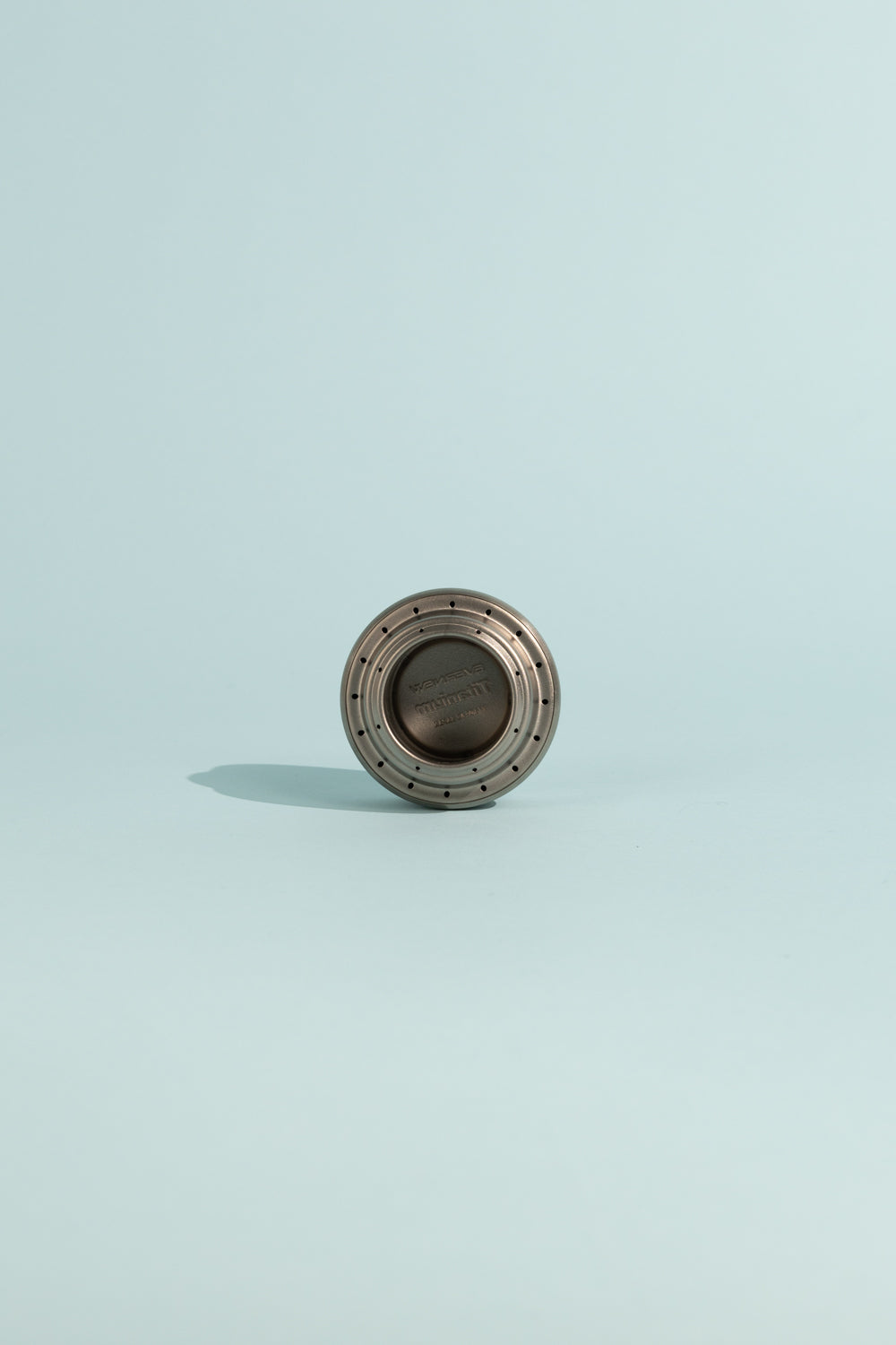 Evernew Titanium Alcohol Stove on a light blue background, showcasing its compact and lightweight design.