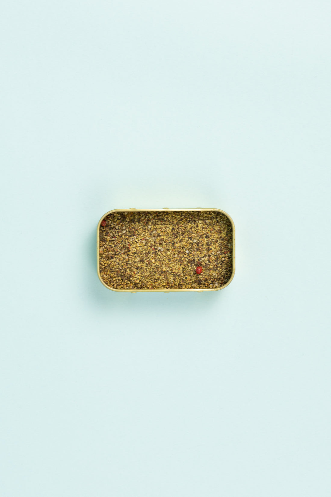 Field Blends Pink Peppercorn, Sea Salt & Garlic camping tin filled with spice blend on light blue background.