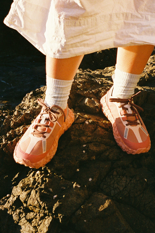 Person wearing 001 - Vermillion shoes standing on a rocky surface, showcasing the unique design and colors.