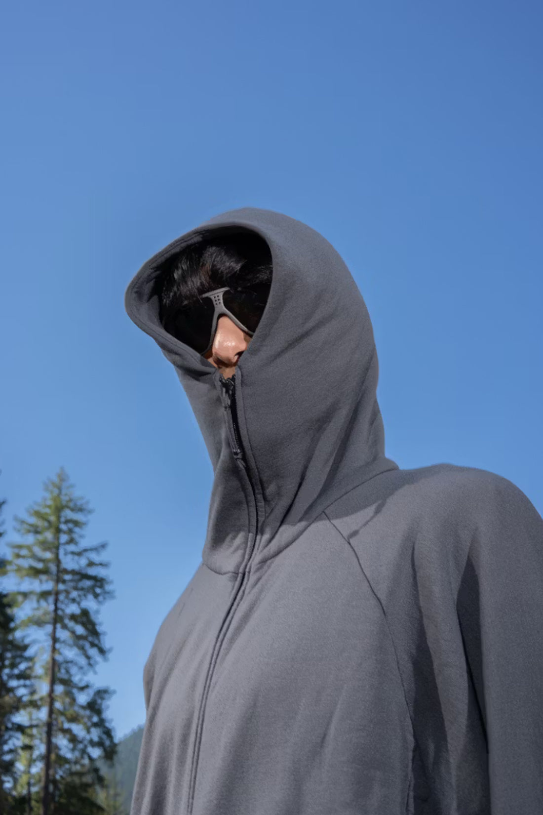 Gnuhr Power Hoodie v1.5 in asphalt worn by a model outdoors with blue sky and trees in the background.
