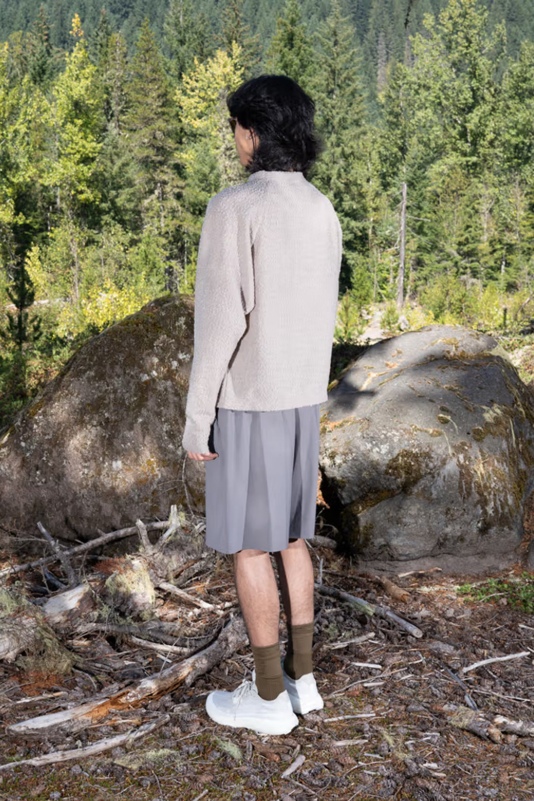 Gnuhr Warp Short Long model wearing charcoal shorts in a forest setting, showcasing innovative pocket design.