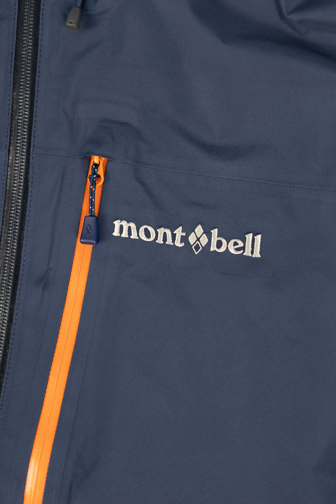 Montbell US Men's Tempest Jacket featuring Montbell logo and bright orange zipper detail in navy color.