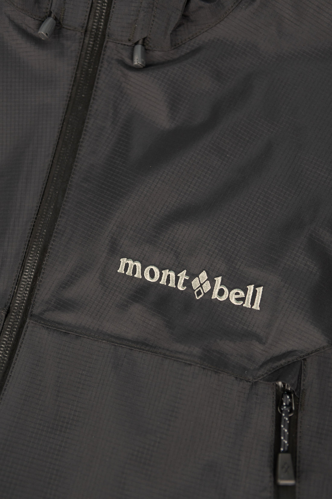 Close-up of Montbell US Men's Rain Trekker jacket in black, showcasing the logo and lightweight fabric.