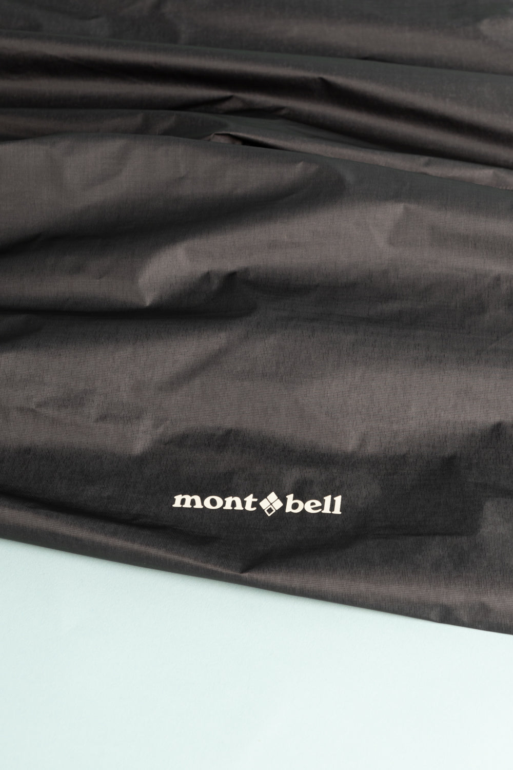Montbell US Men's Dry-Tec U.L. Rain Pants in black material showcasing Montbell logo on a textured surface.