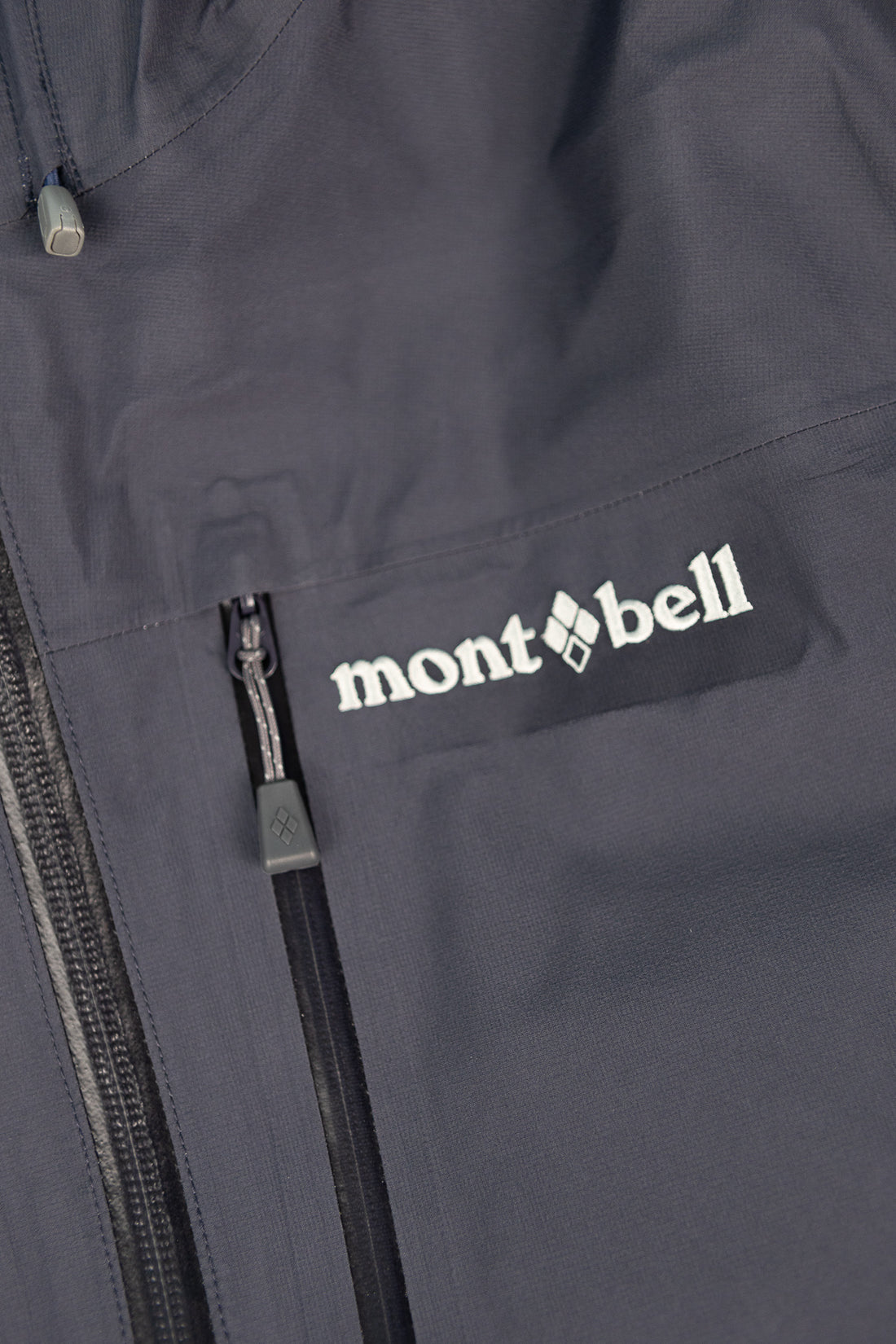 Close-up of the Montbell US Women's Tempest Jacket in navy showing the logo and zipper details.