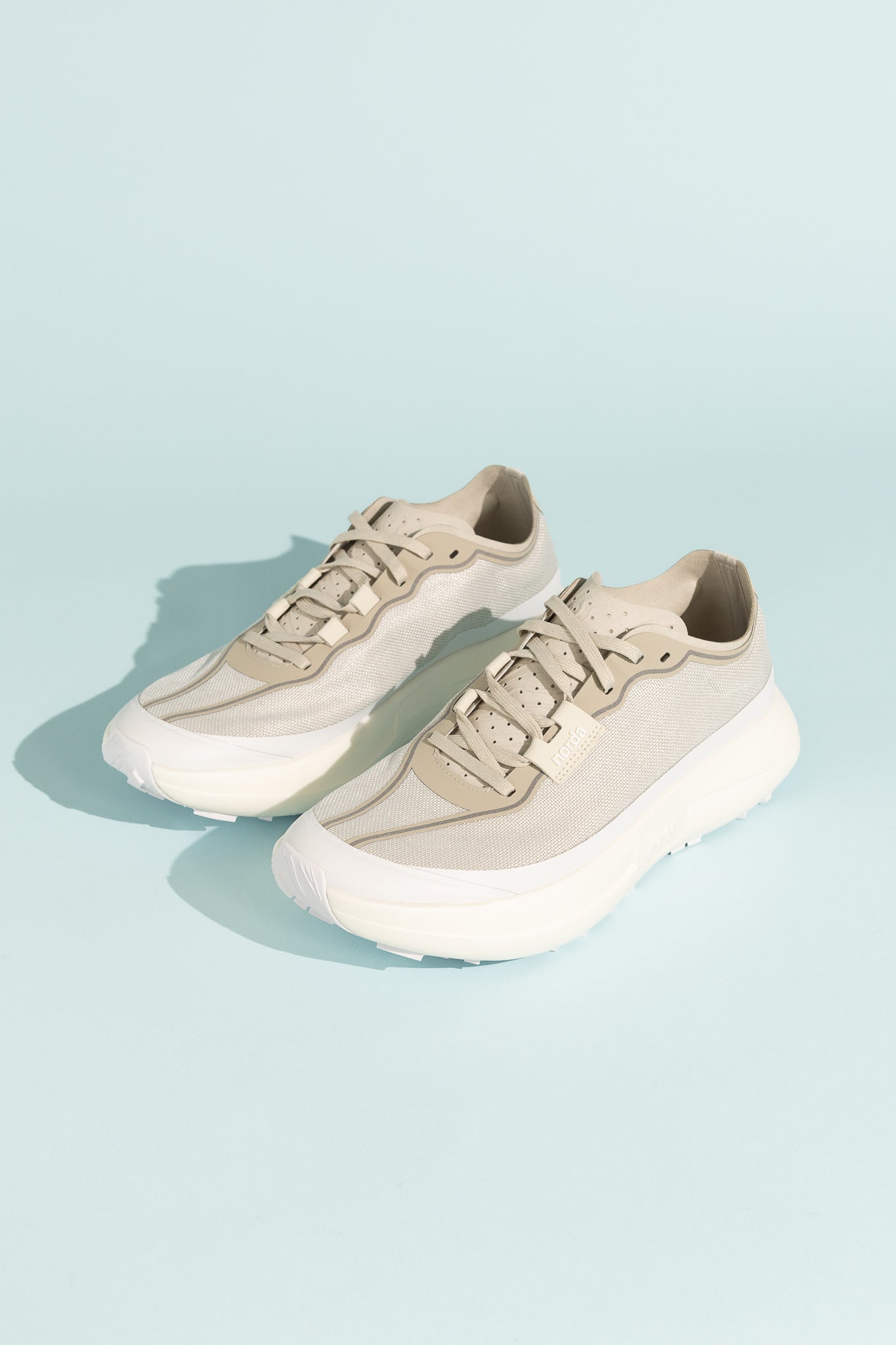 Norda 005 - Névé lightweight trail shoes with open-mesh upper and cushioned soles on a blue background.