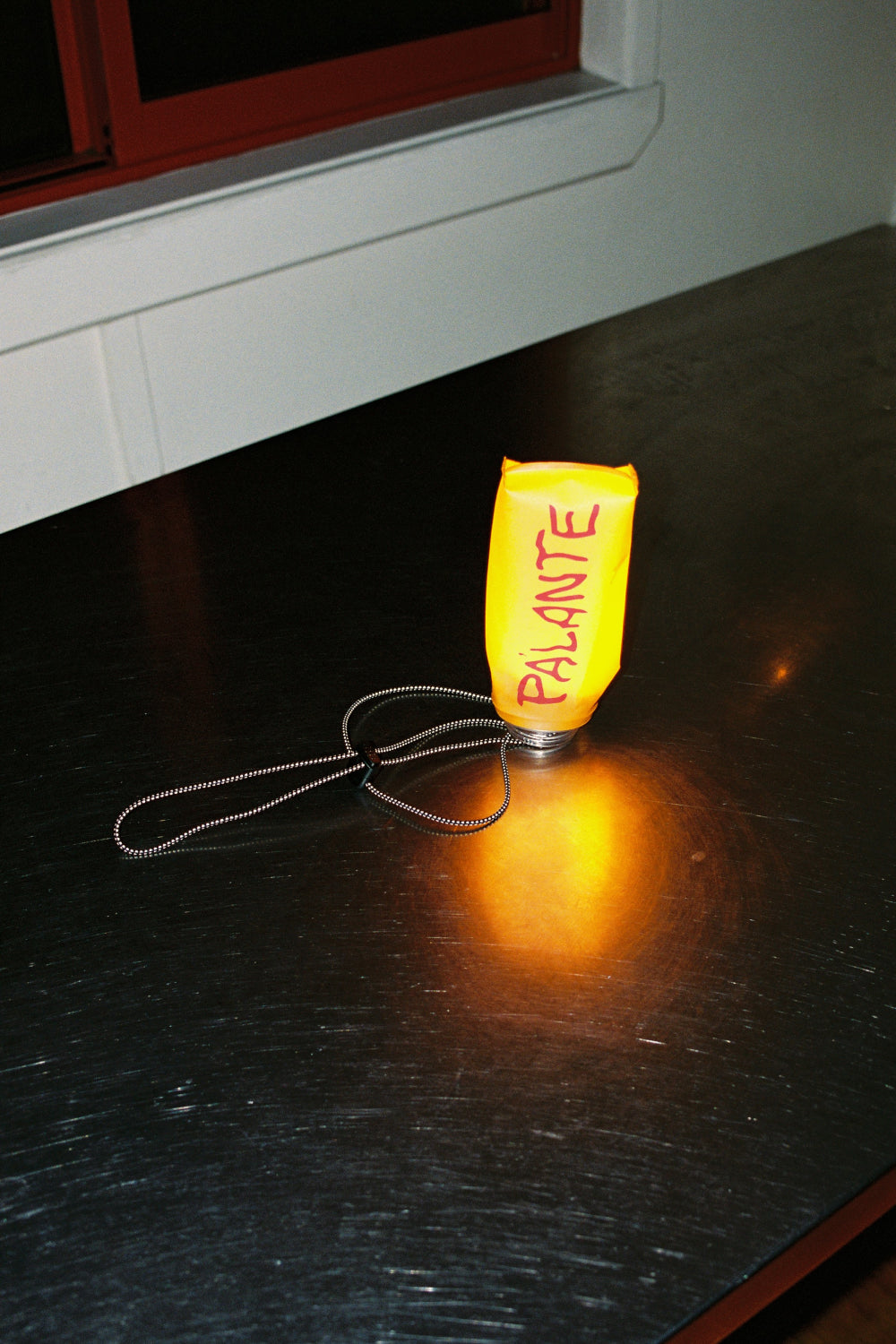 Pa'lante Floppy Water Bottle in bright orange on a table with a light, showcasing its reusable and collapsible features.