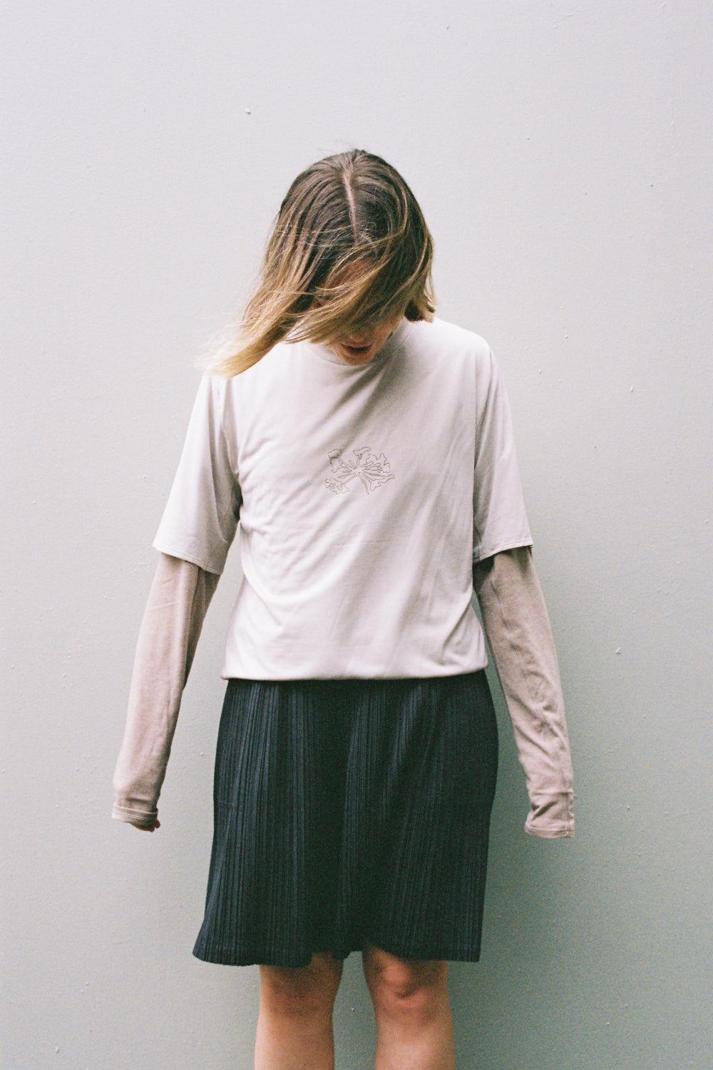 Model wearing the Portal Lateral Peak Tee - Bone White combined with a long-sleeve top and a skirt, showcasing an active lifestyle.