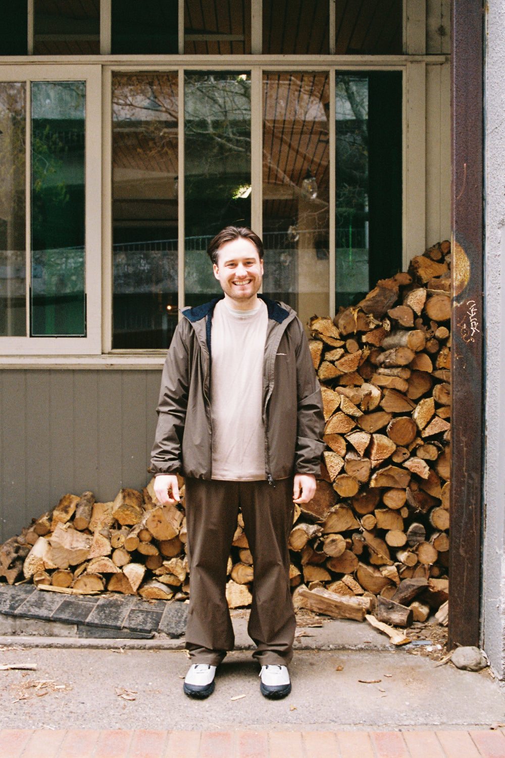 Man wearing Portal Level Alpha Jacket - Slate Black standing in front of a woodpile.
