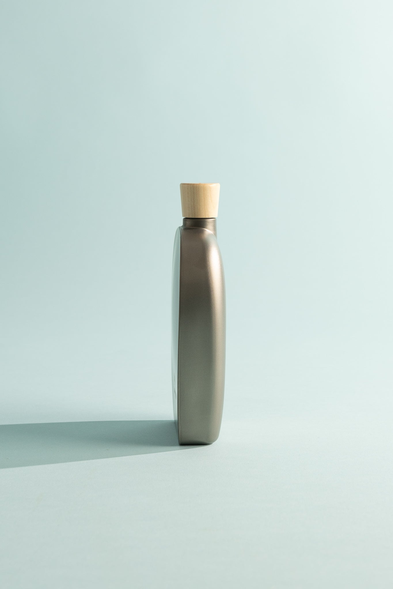 Side view of Snow Peak 250ml Titanium Flask with wooden cap against a light blue background.