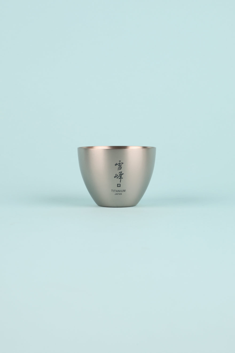 Snow Peak Titanium Sake Cup on a light blue background, showcasing its elegant design and premium titanium finish.