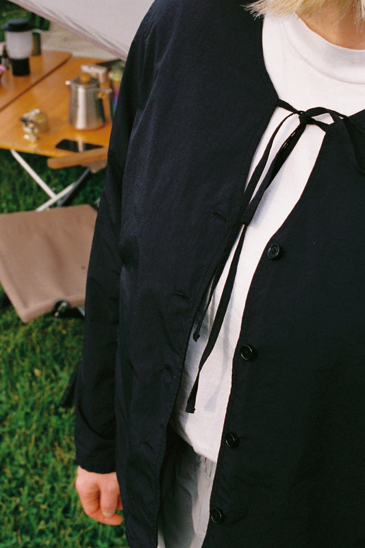 Person wearing a Garment Dyed Blouse in black, styled with a light top, outdoors on green grass.