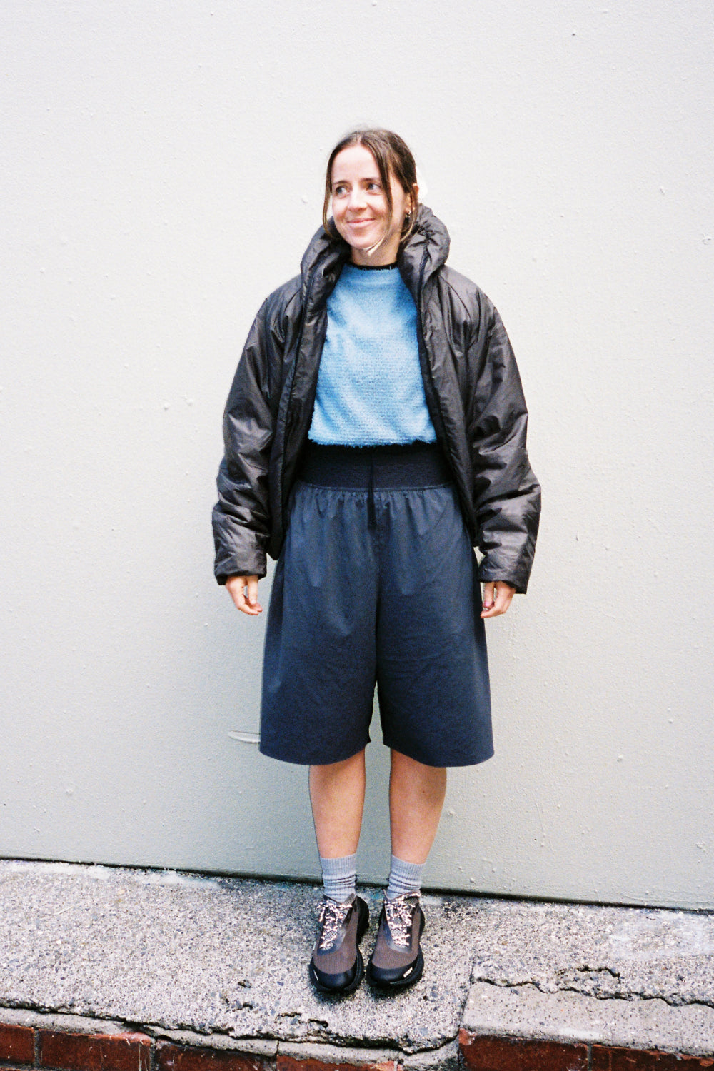 Model wearing Heatwave Puffer Jacket in Major Brown, styled with a blue top and dark shorts.