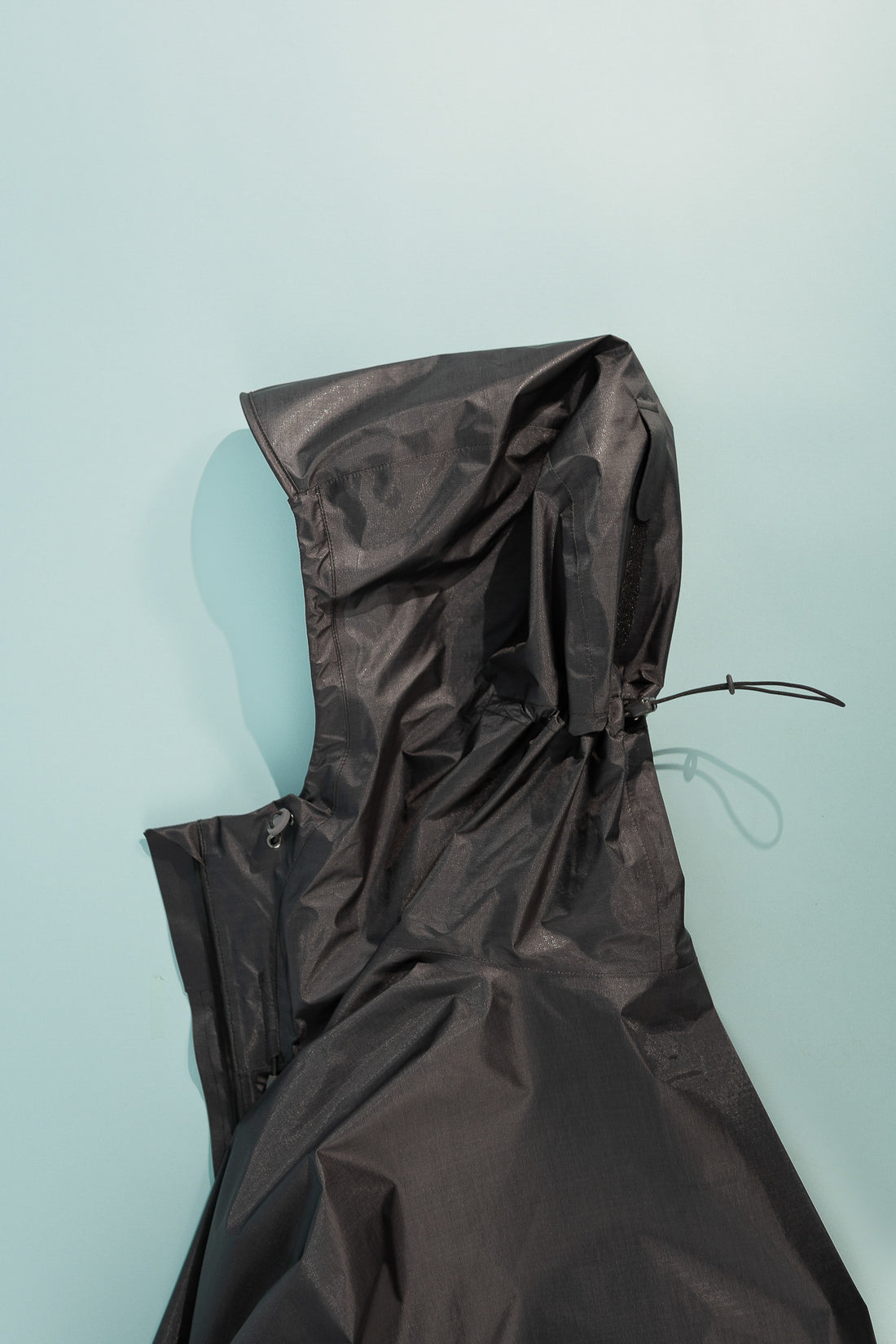 US Men's Versalite Jacket - Black fabric hood against a blue background, showcasing ultralight rain shell design.