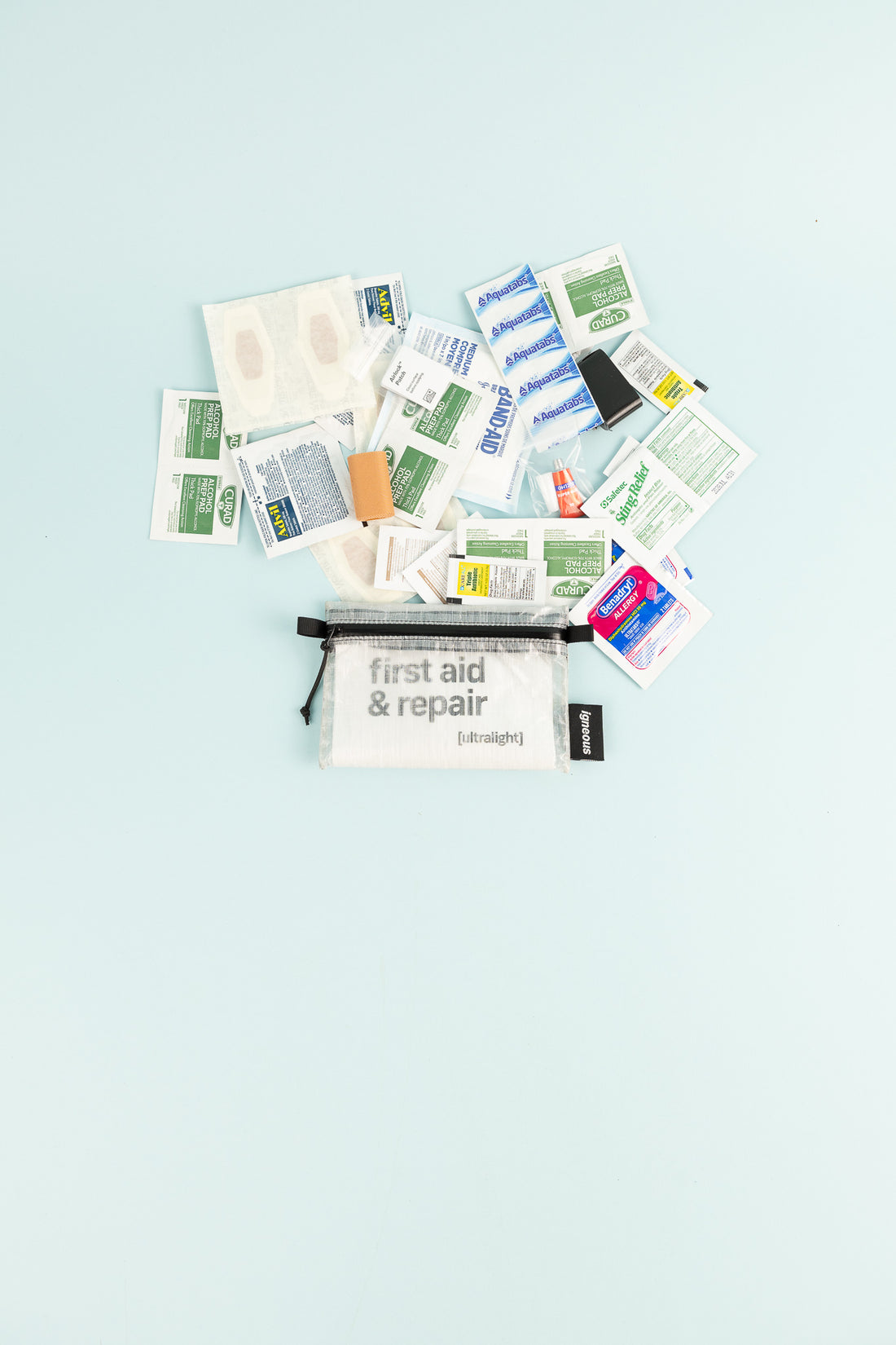 First Aid + Repair Kit with various medical supplies scattered on a light background.