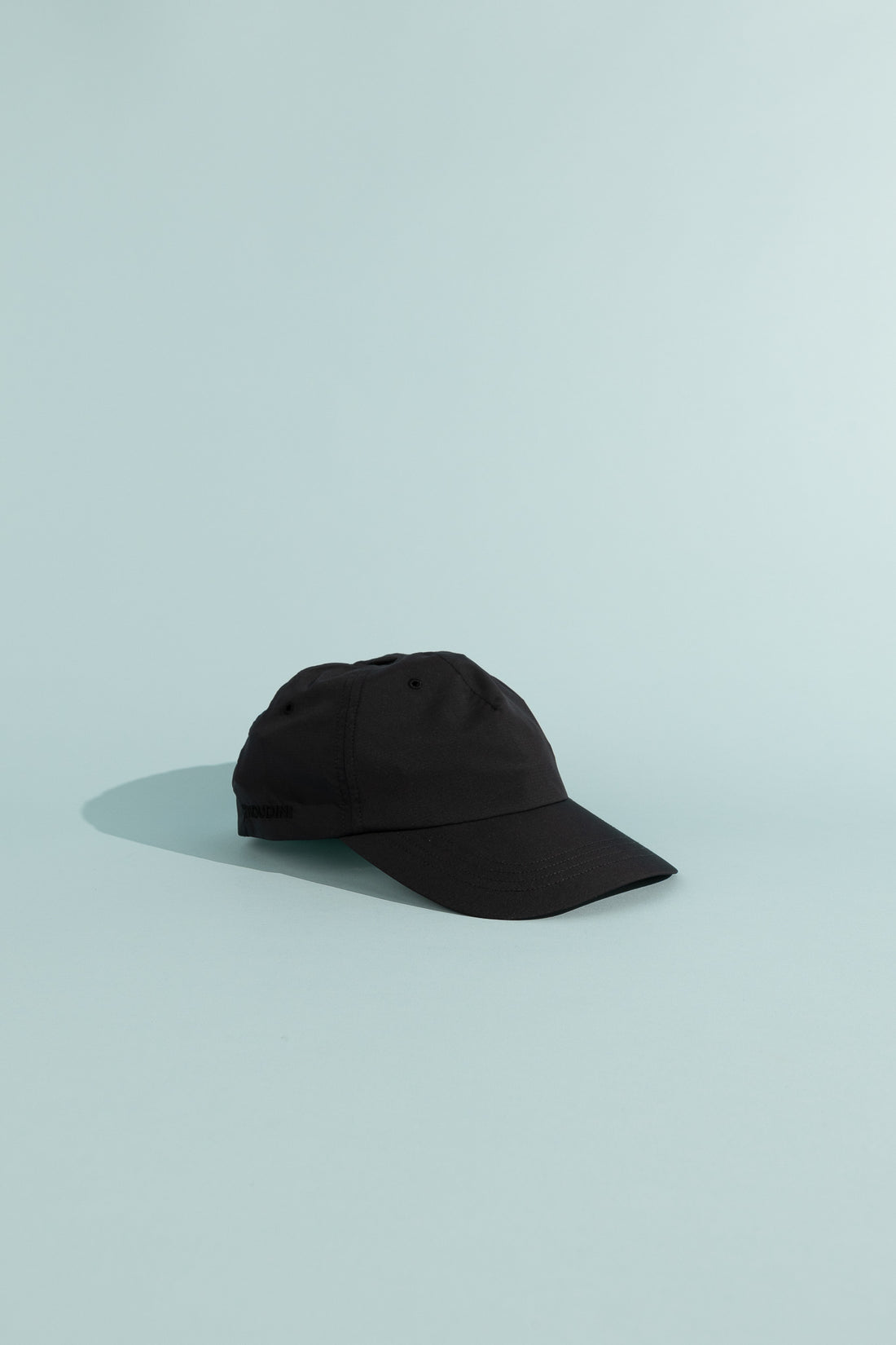 C9 Cap - True Black displayed on a light blue background, showcasing its lightweight, breathable design.