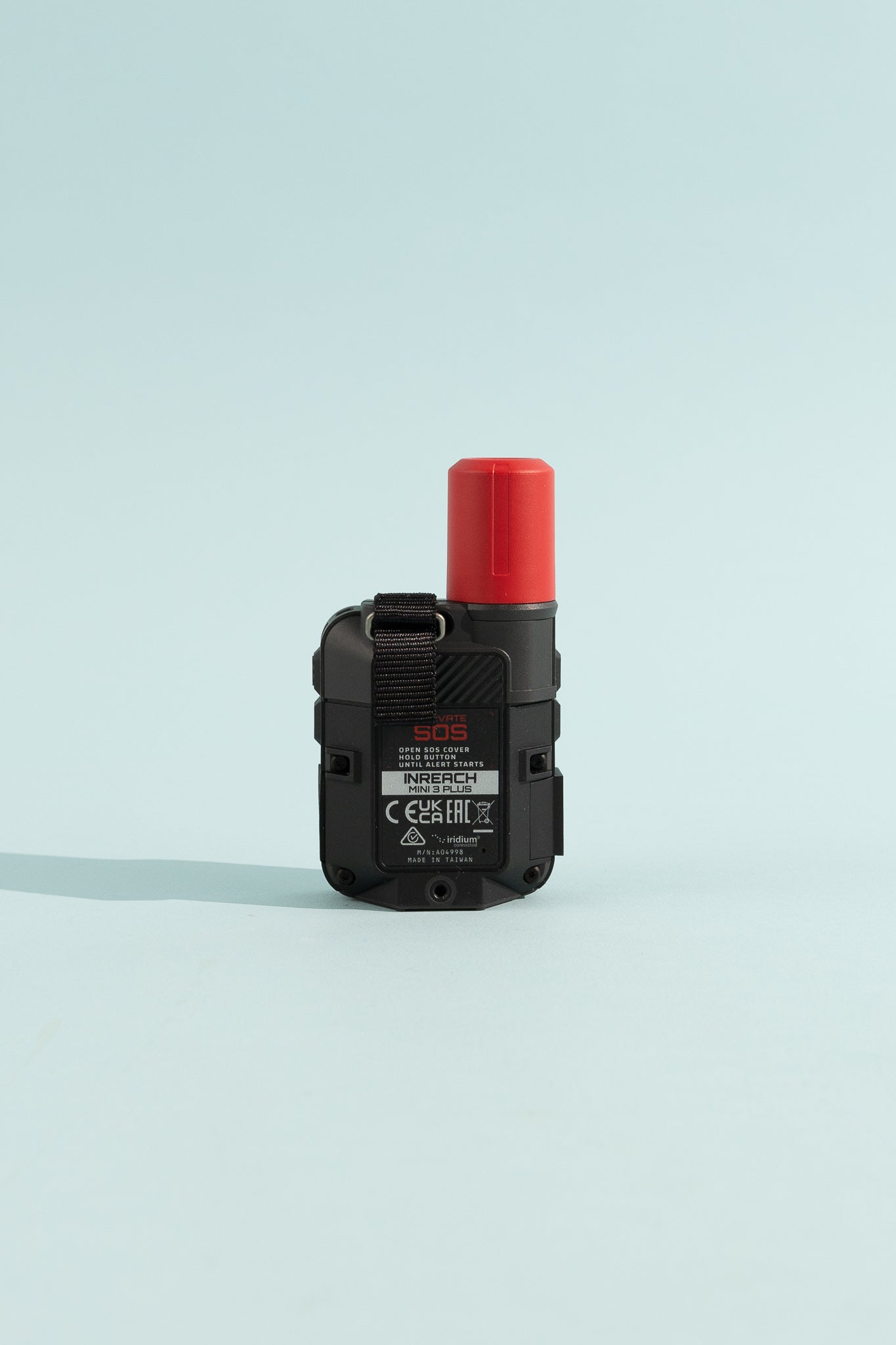 Garmin inReach Mini 3 Plus back view featuring black design and red SOS button on a light blue background.