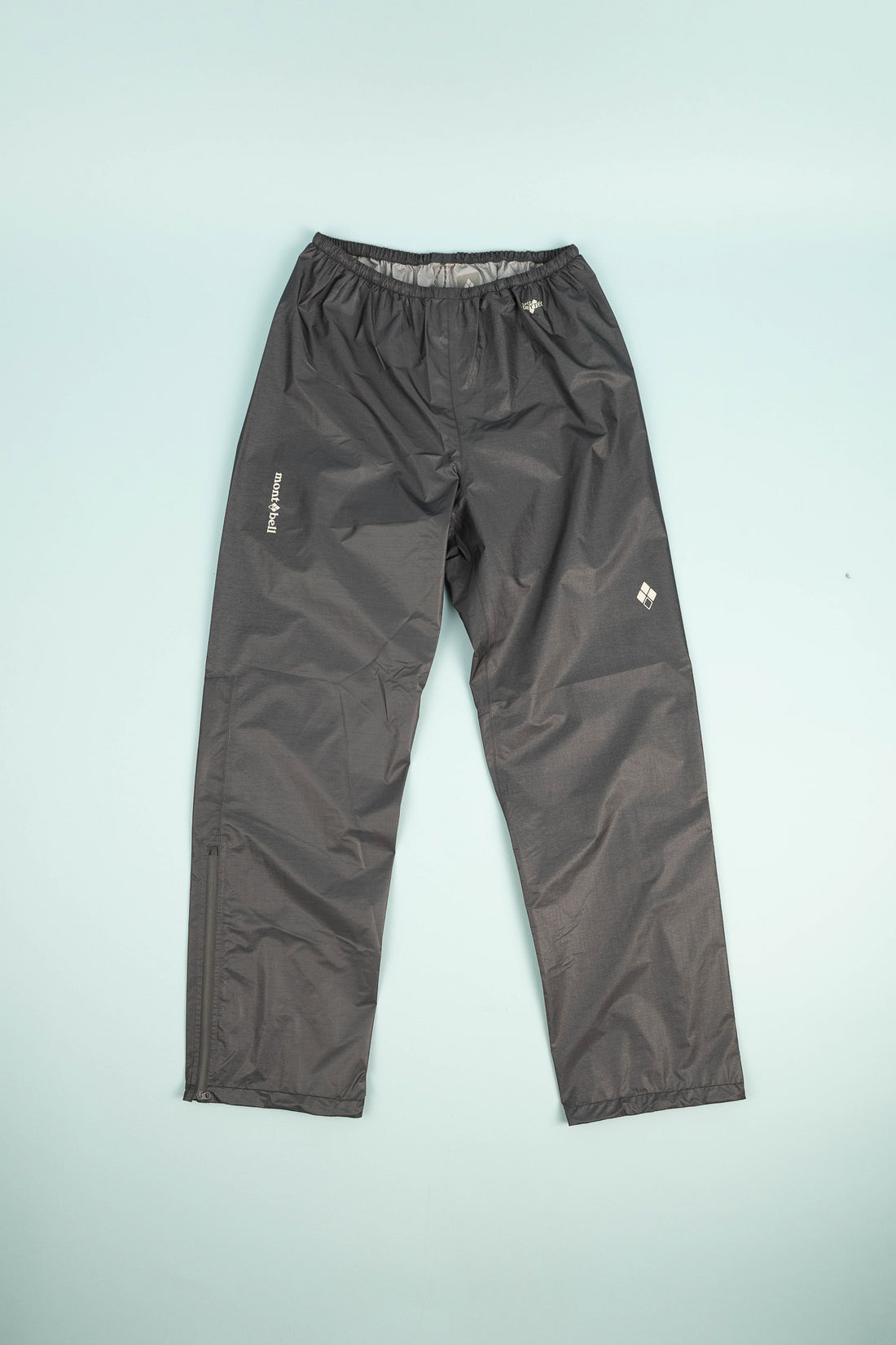 Montbell US Women's Dry-Tec U.L. Rain Pants - Dark Gray on a light blue background.