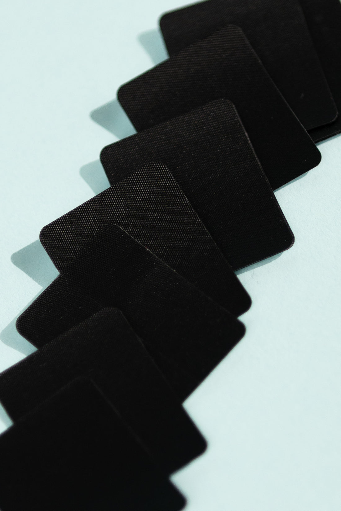 Set of black Igneous Threadlock Patches arranged on a light blue background for repairing technical fabrics.