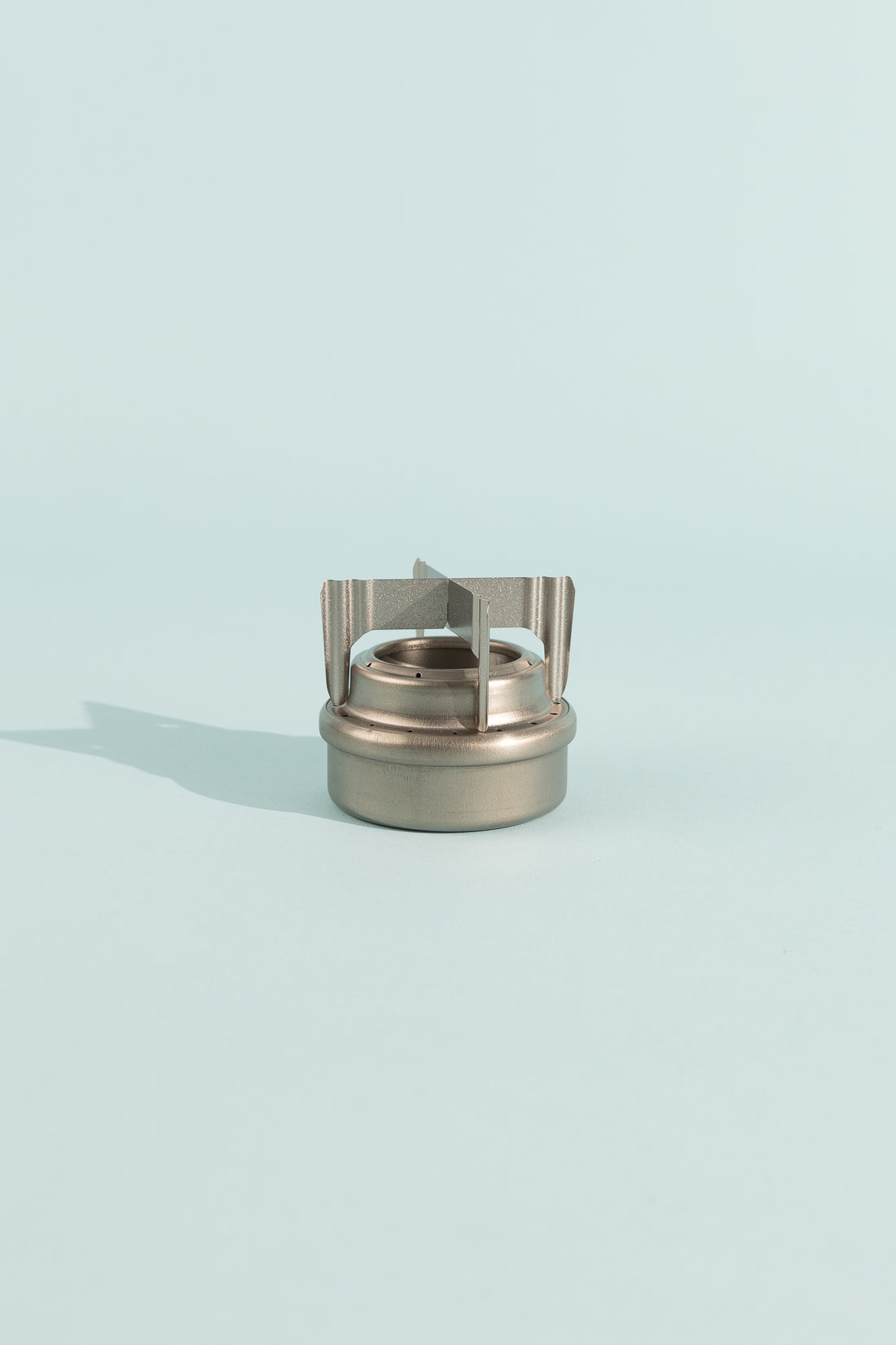 Evernew T0.3 TriveTi compact camping stove with a sleek silver design on a light blue background.