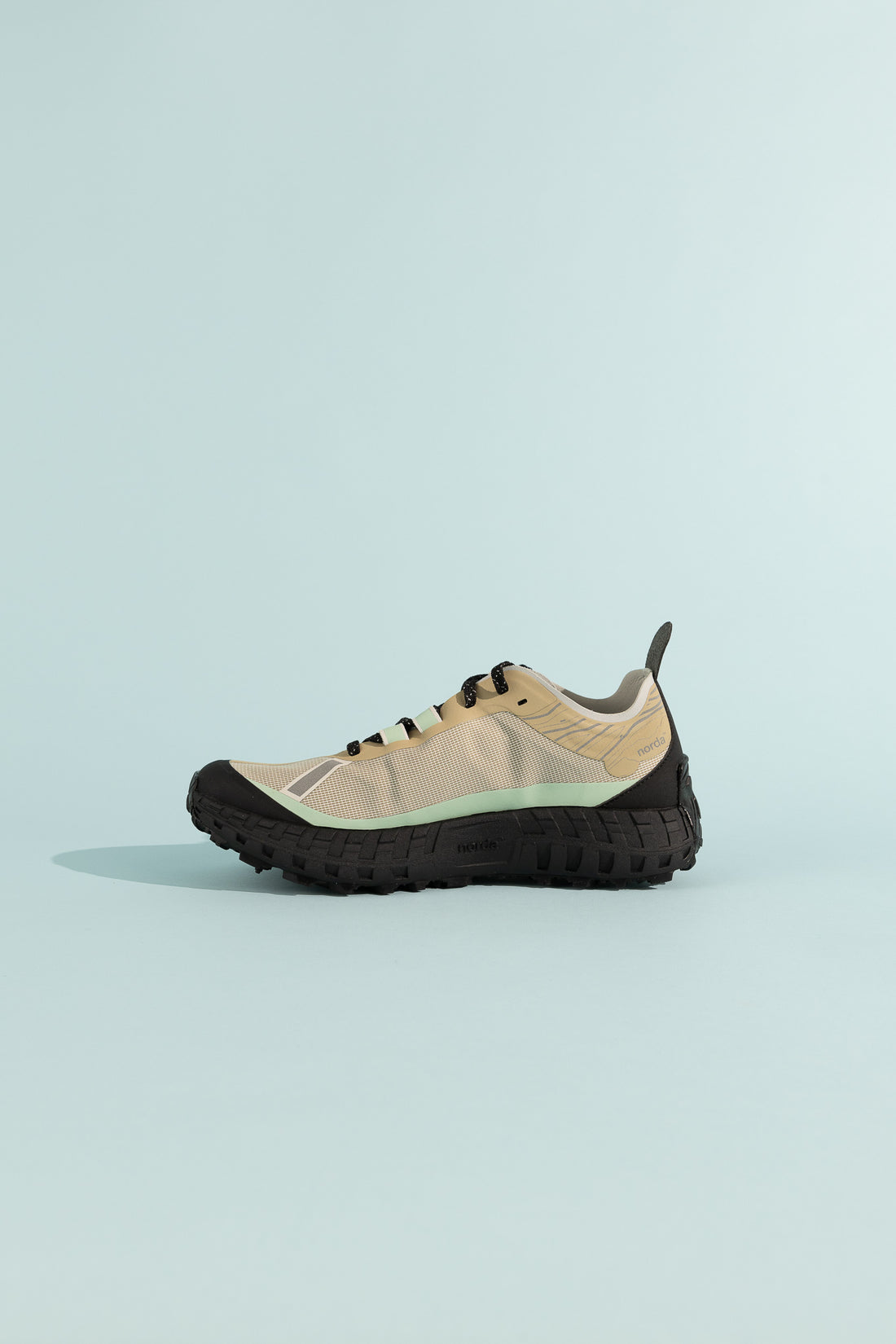 001A - Astral shoe in beige with black sole on a light blue background, showing a side view.