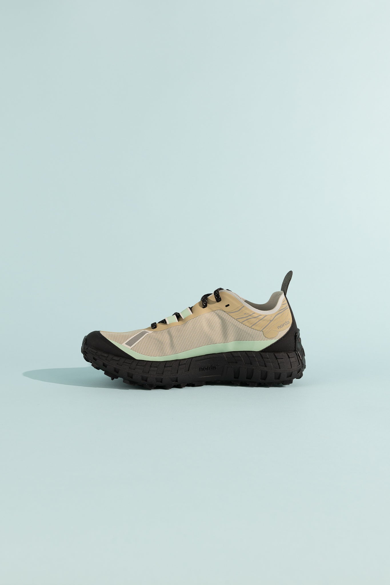001A - Astral shoe in beige with black sole on a light blue background, showing a side view.