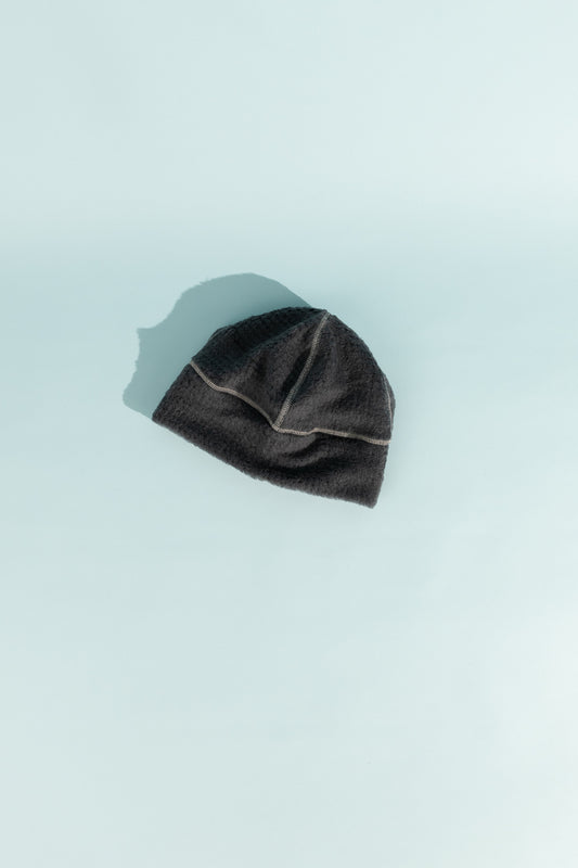 High Loft Wool Beanie in anthracite and glacier grey resting on a light blue background.
