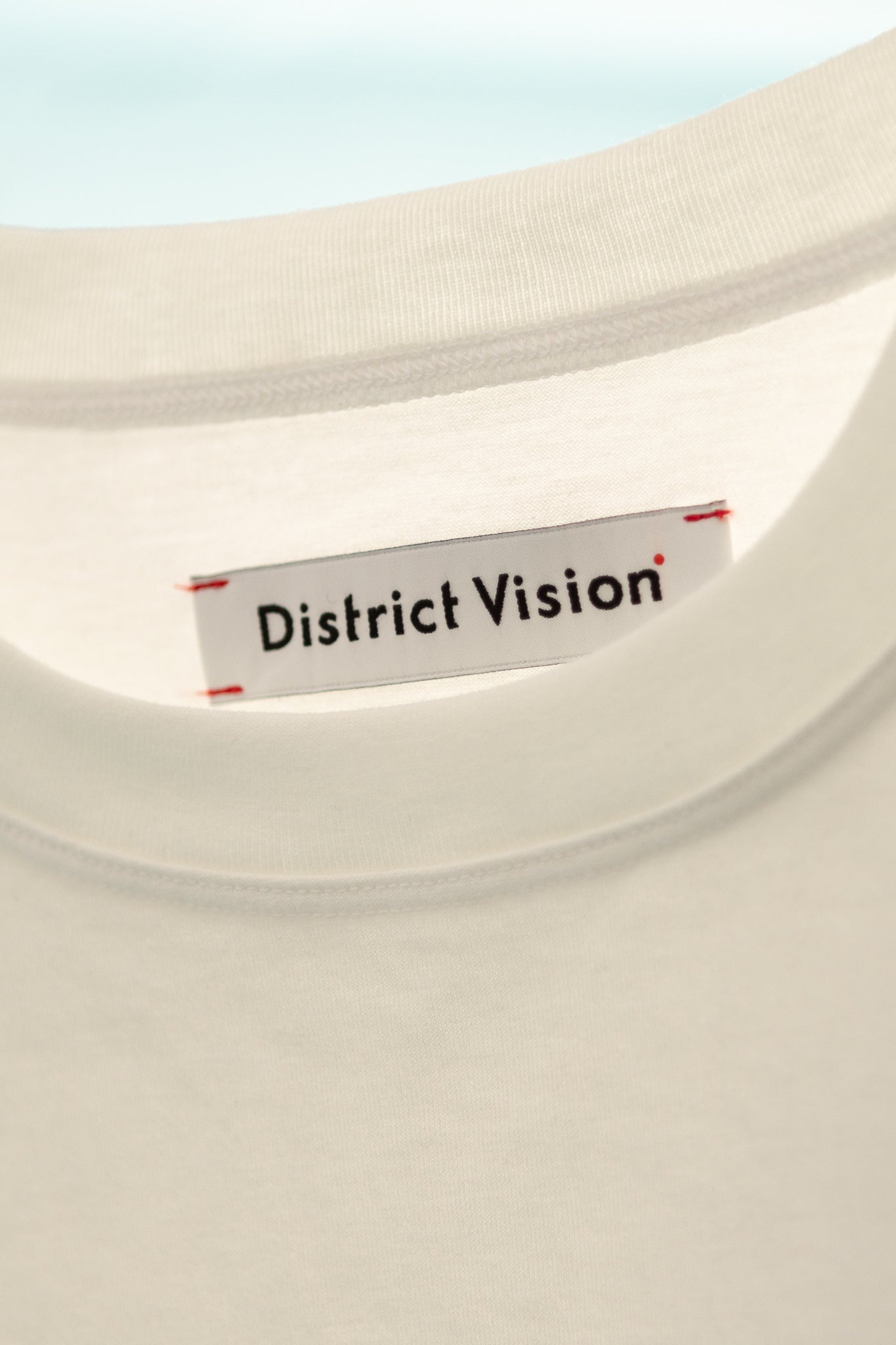 Close-up of the label on the District Vision Womens Fitted Cropped T-Shirt in off white, showcasing brand logo.