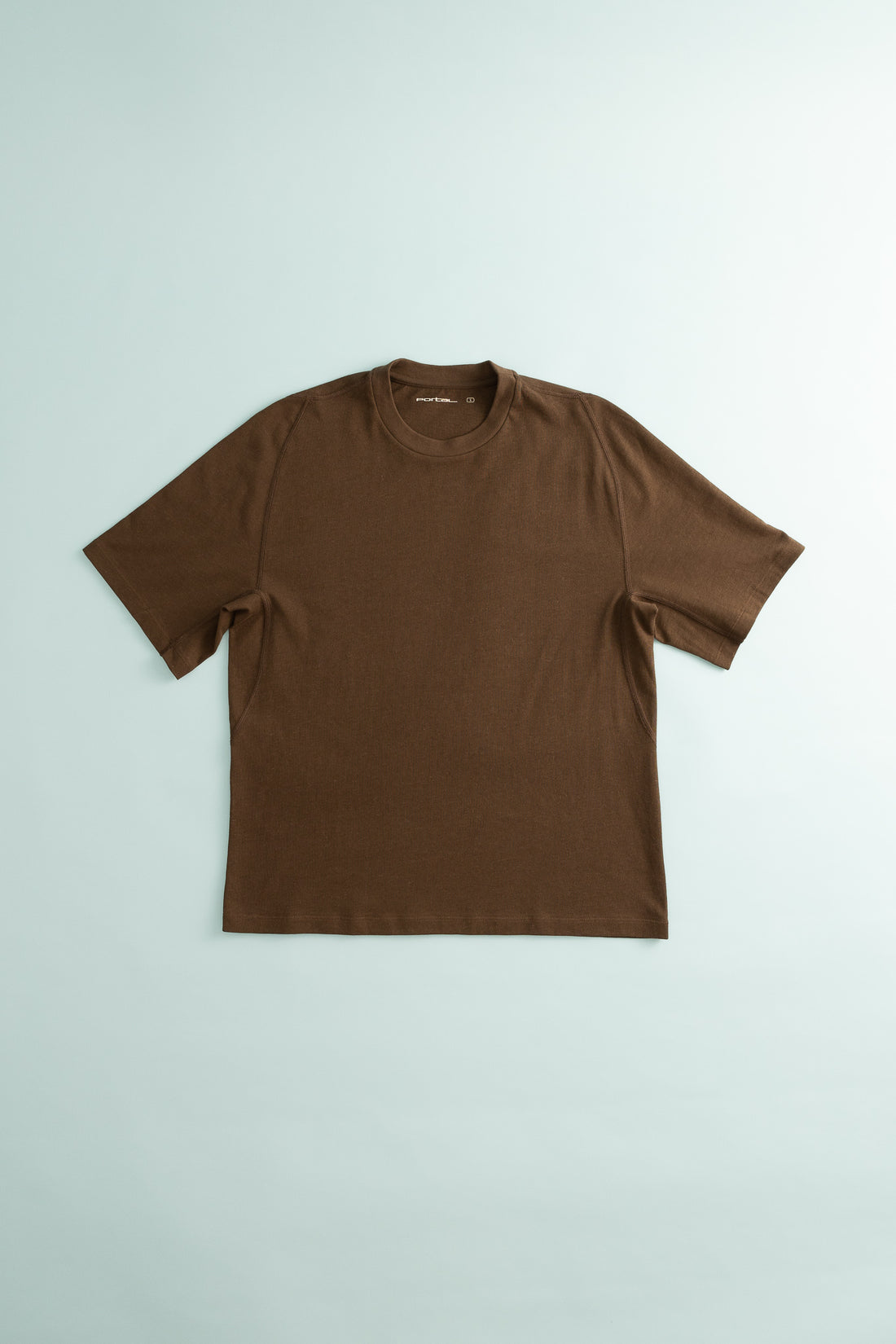 Root Hemp Tee in brown color displayed on a light blue background, showcasing its comfortable design.