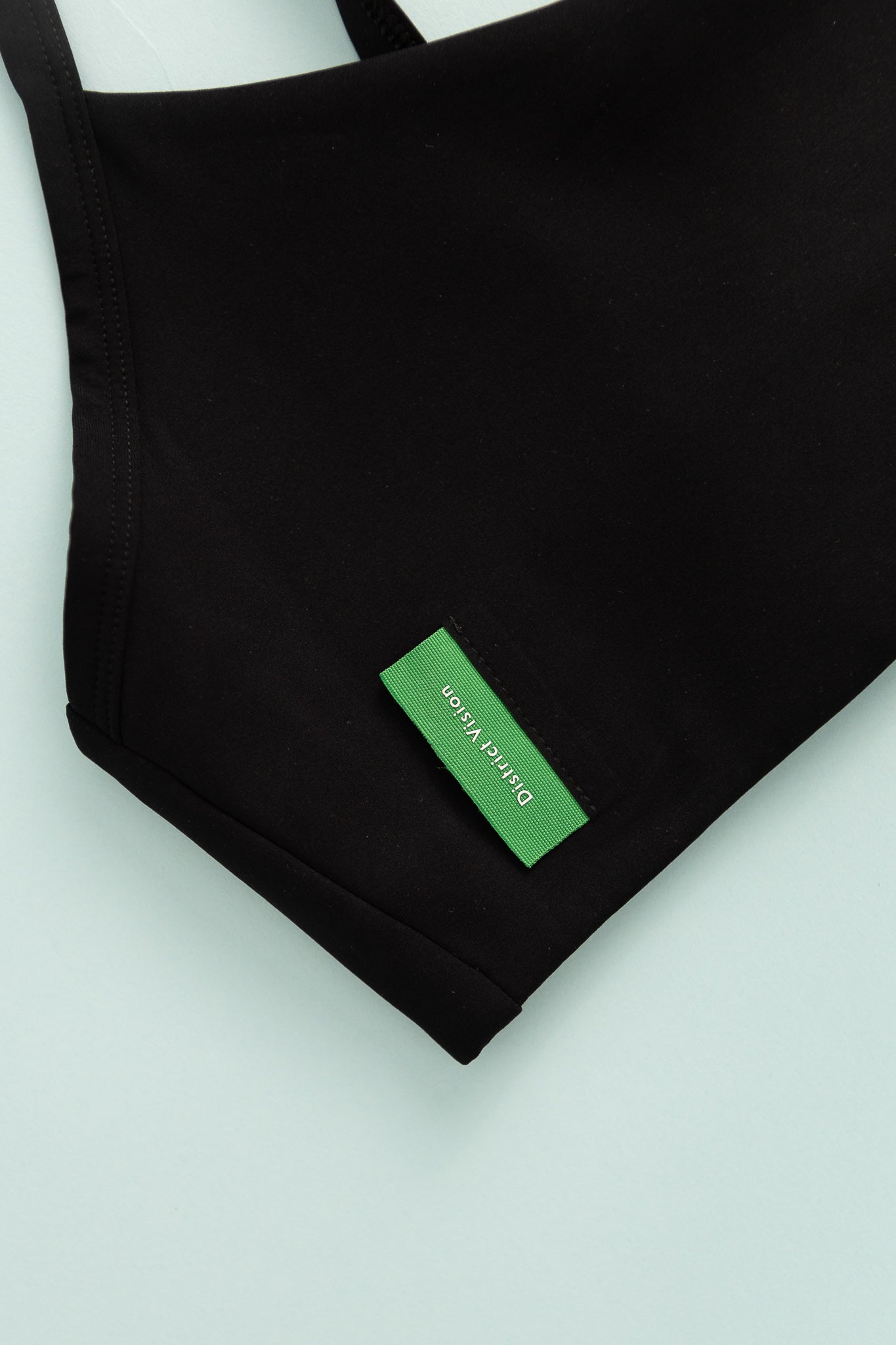 District Vision Womens Light Support Interlock Bra in black fabric with green logo tag.